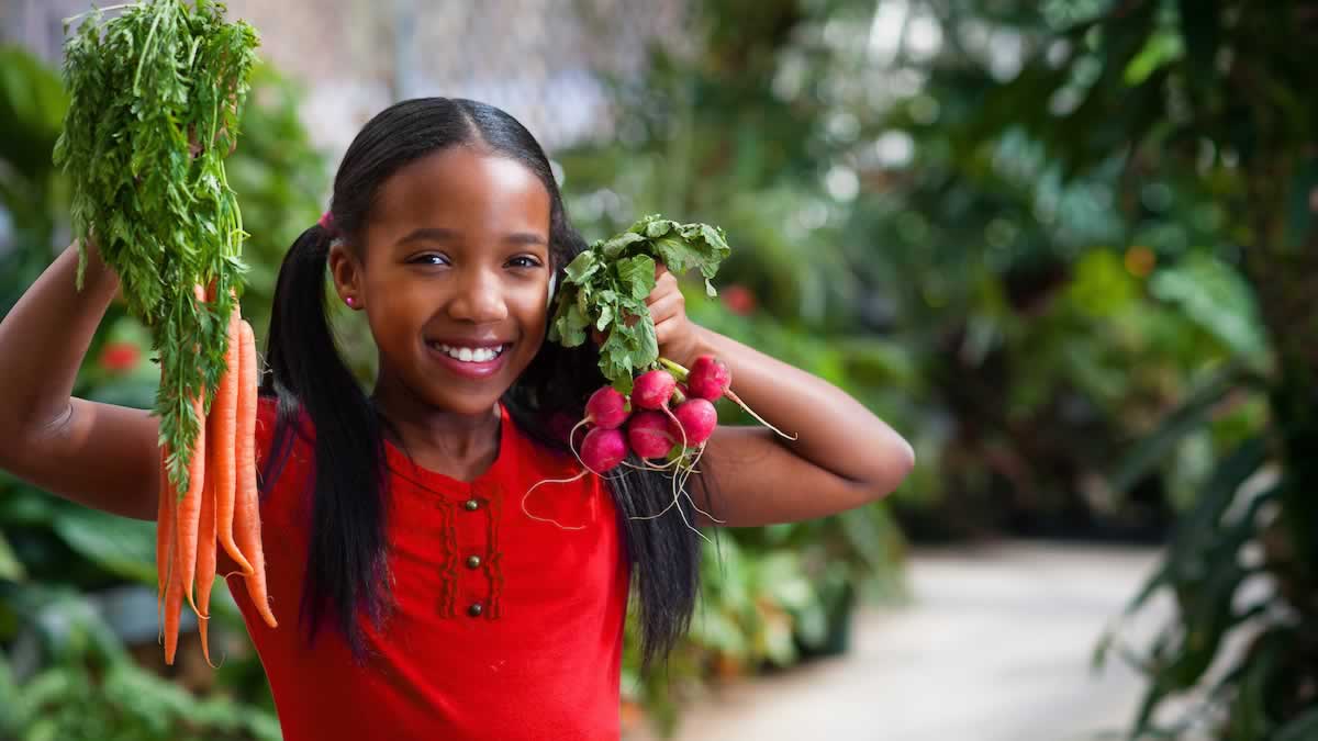 young girl holding fresh carrots and radishes